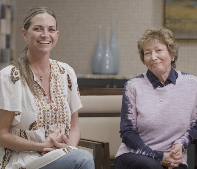 Senior woman and her adult daughter smile and sit in chairs for an interview