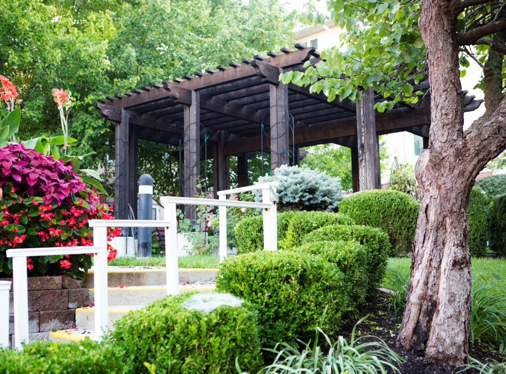 steps leading up to a wooden arbor and fountain at Claridge Court, lined with bright green bushes, flowers, and trees