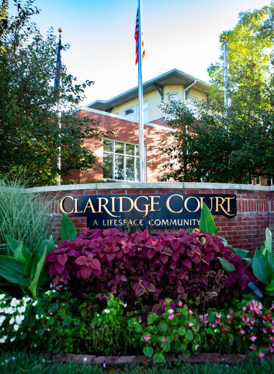 Claridge Court Senior Living Community's brick entrance sign with floral landscape and gold lettering depicting the name