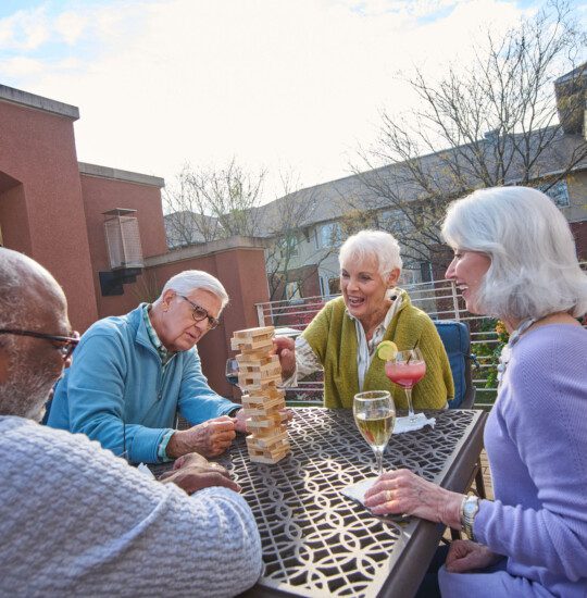 group of seniors play Jenga and enjoy drinks together in a sunny courtyard terrace