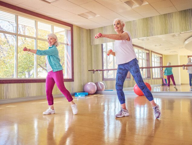group of seniors smile and lift weights during an aerobics class