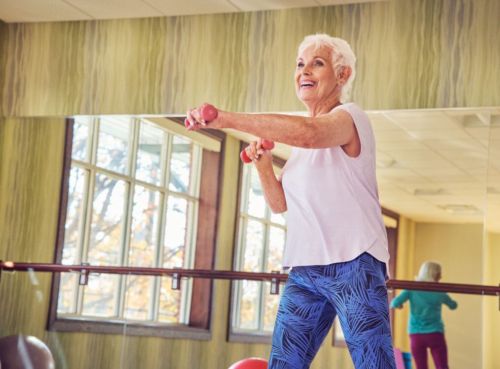 group of seniors smile and lift weights during an aerobics class