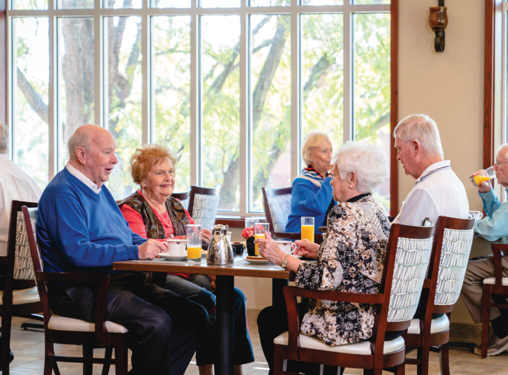 group of seniors sit at a table in a casual dining space for brunch together at Claridge Court Senior Living Community