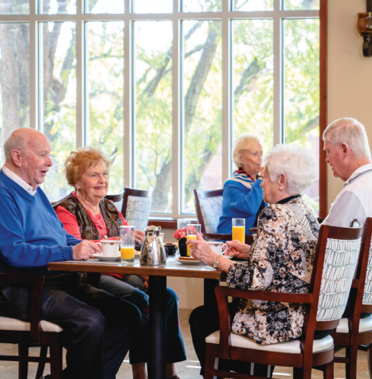 group of seniors sit at a table in a casual dining space for brunch together at Claridge Court Senior Living Community