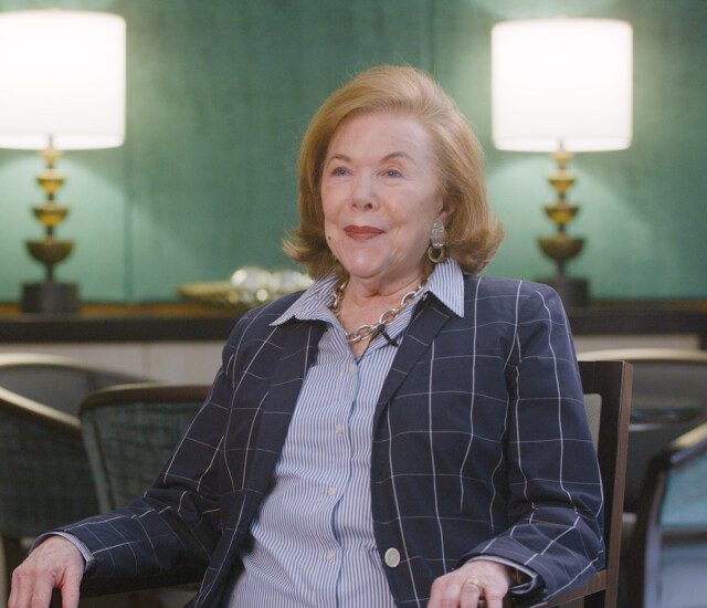 Senior woman in blazer sits in chair for an interview