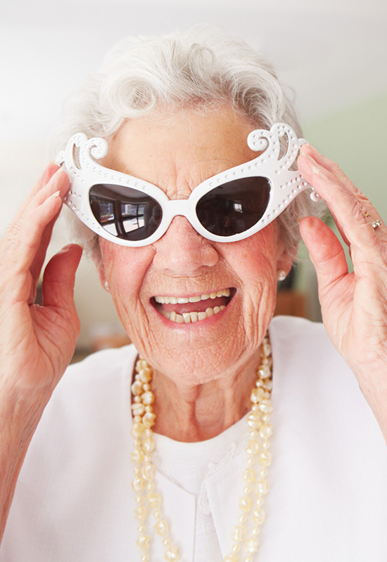 senior woman wearing white party glasses smiles into the camera