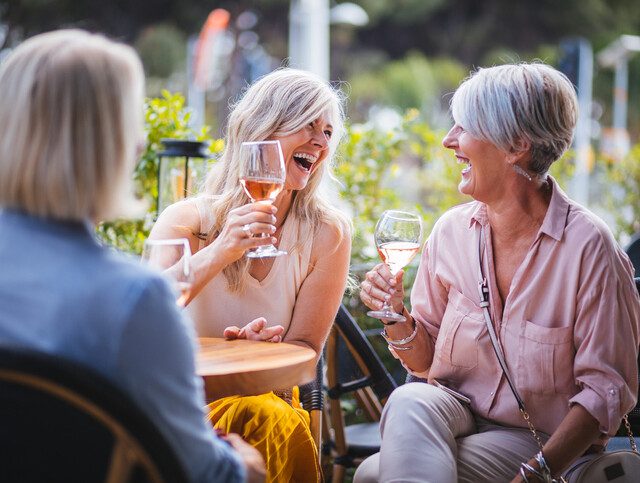 Mature women enjoying a glass of wine, having fun and laughing together at city restaurants.