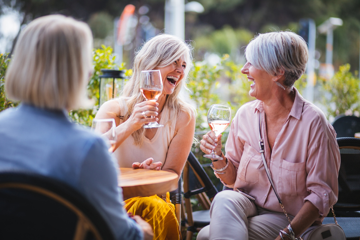 Mature women enjoying a glass of wine, having fun and laughing together at city restaurants.