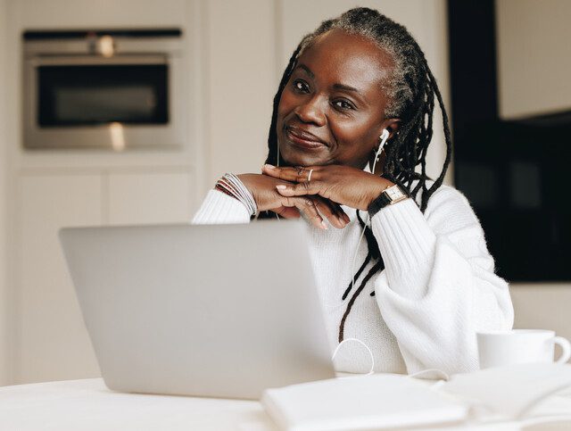 Senior woman smiling at the camera with a laptop computer in front of her.