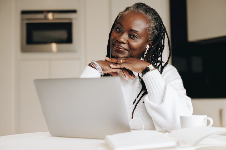 Senior woman smiling at the camera with a laptop computer in front of her.