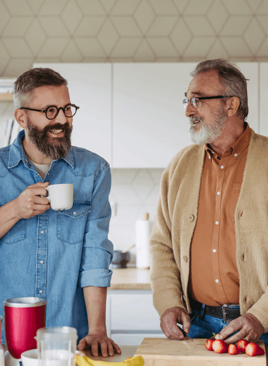 Two men share a moment over coffee and fruit preparation in a kitchen setting.