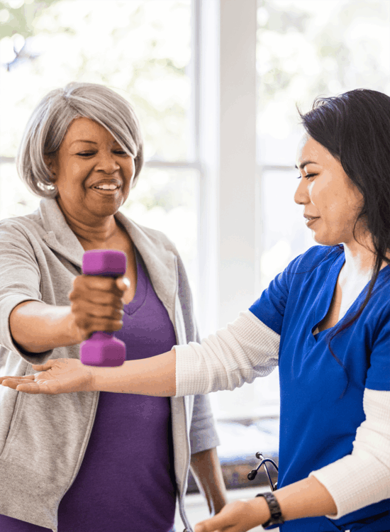 A caregiver assists an older woman with exercise using weights indoors.